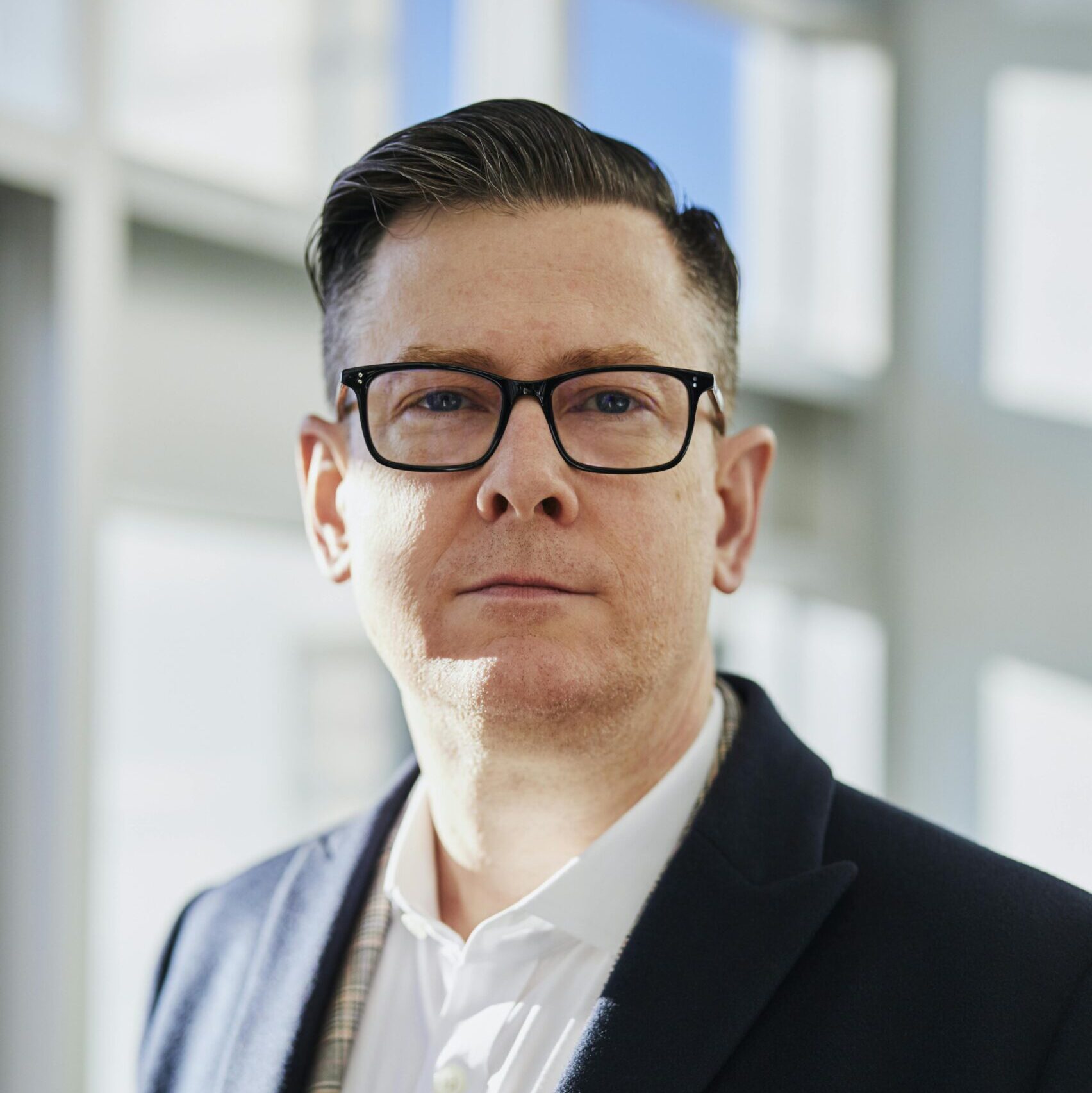 Profile portrait of a confident business executive wearing eyeglasses in a sunlit office setting.